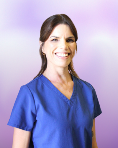 A woman wearing blue medical scrubs stands smiling in front of a purple gradient background.
