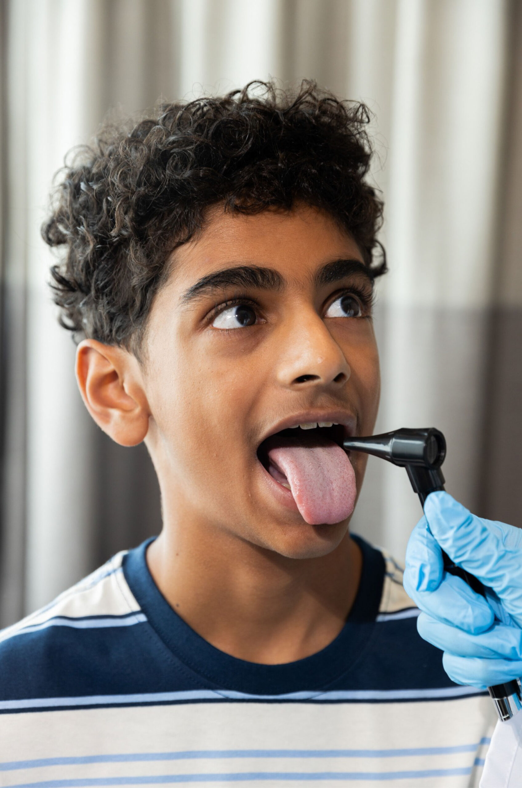 A healthcare professional in blue gloves examines a boy’s throat with a medical instrument, while nearby, his insurance information is reviewed.